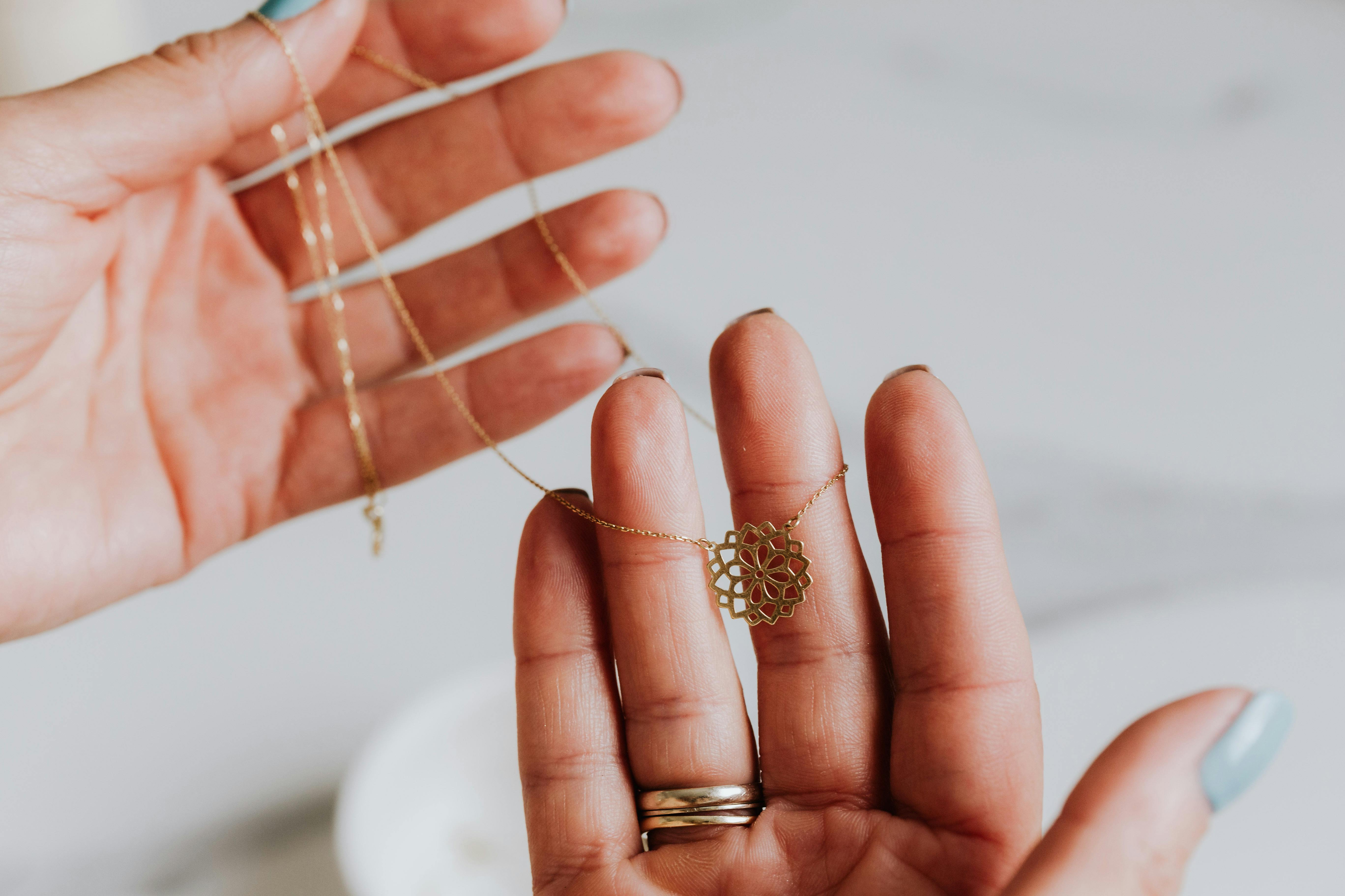 gold necklace with flower pendant on human fingers