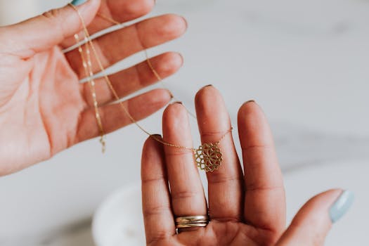 Close-up of a delicate gold necklace being held between hands, featuring an intricate pendant design.