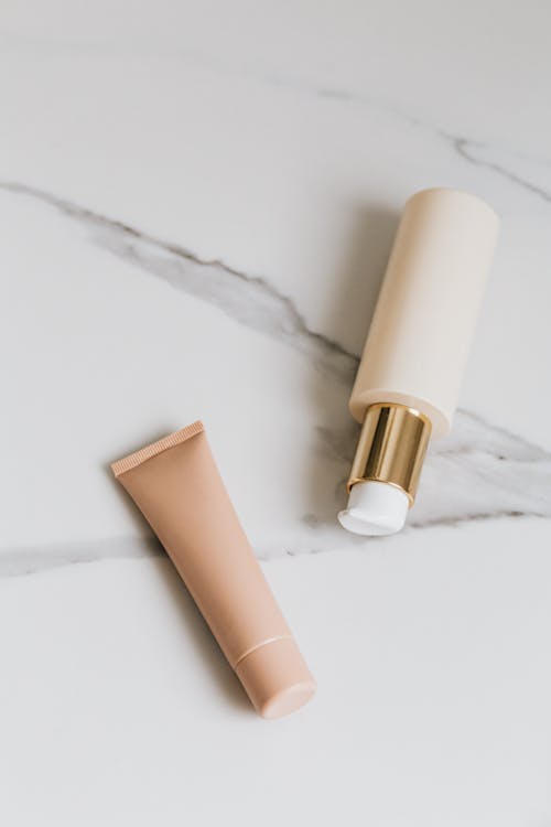 Brown Cream Tube and Pump Bottle on White Surface
