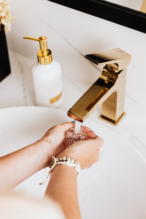 Free Elevated view of hands washing under a gold faucet in a modern bathroom, promoting cleanliness and hygiene. Stock Photo