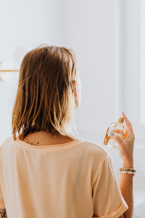 Free Back view of a woman spraying perfume with a serene minimalist background. Stock Photo