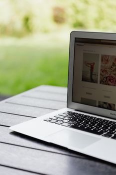 Close-up of an open laptop on a table displaying a website outdoors.