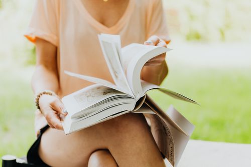 Free A woman enjoys reading a book in a serene outdoor setting, turning its pages. Stock Photo