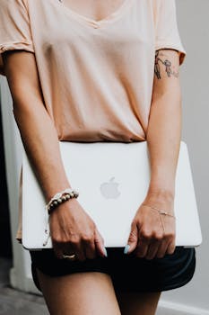 A woman in casual attire holds a laptop, showcasing modern and relaxed lifestyle.