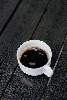 特写镜头中，一杯热浓咖啡置于纹理木桌上的白色杯子里，营造出清爽的氛围