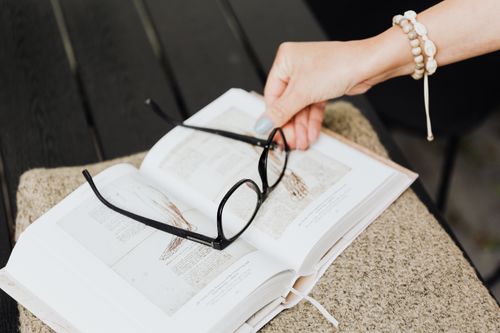 Free A hand holding eyeglasses over an open book outside on a sunny day. Stock Photo