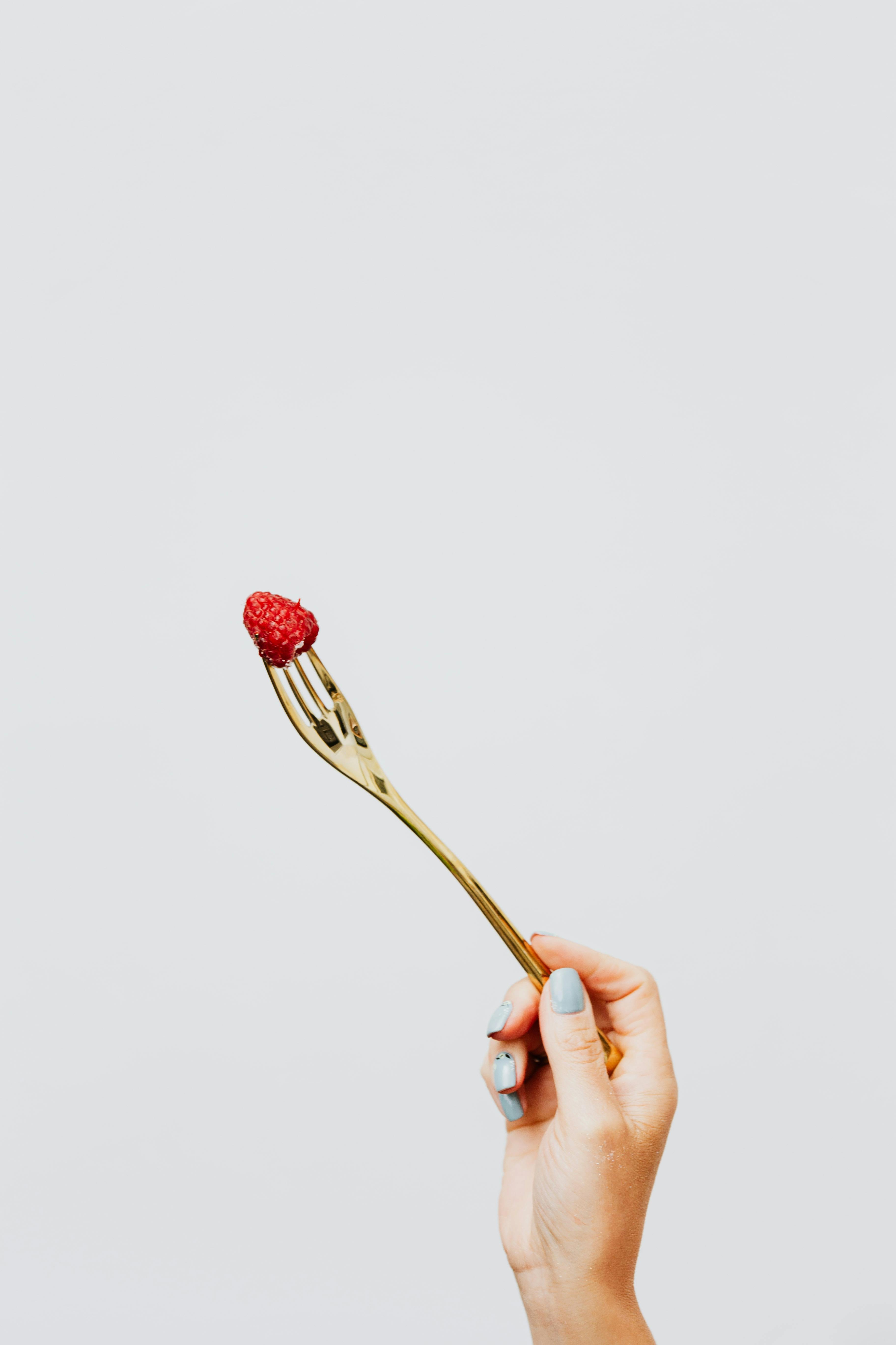 A minimalist shot of a hand holding a fork with a raspberry, showcasing copy space.
