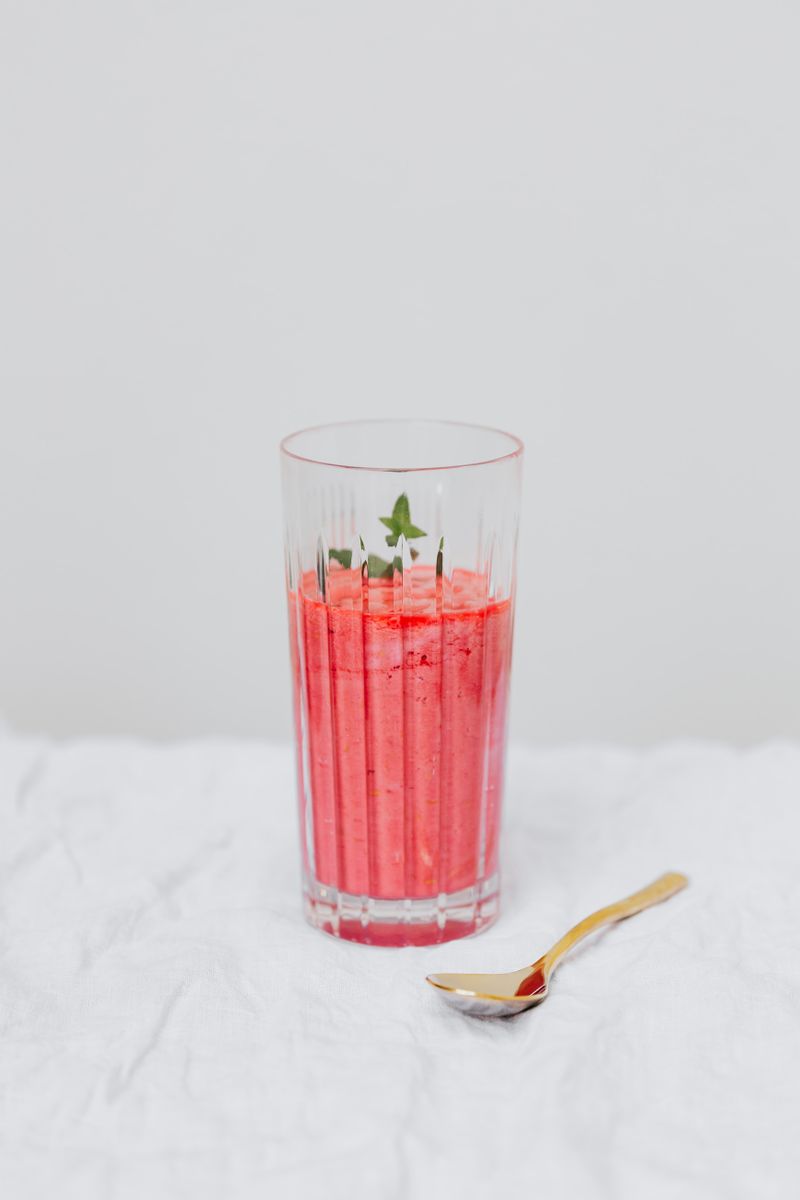 Vibrant strawberry smoothie served in a clear glass with a mint garnish.