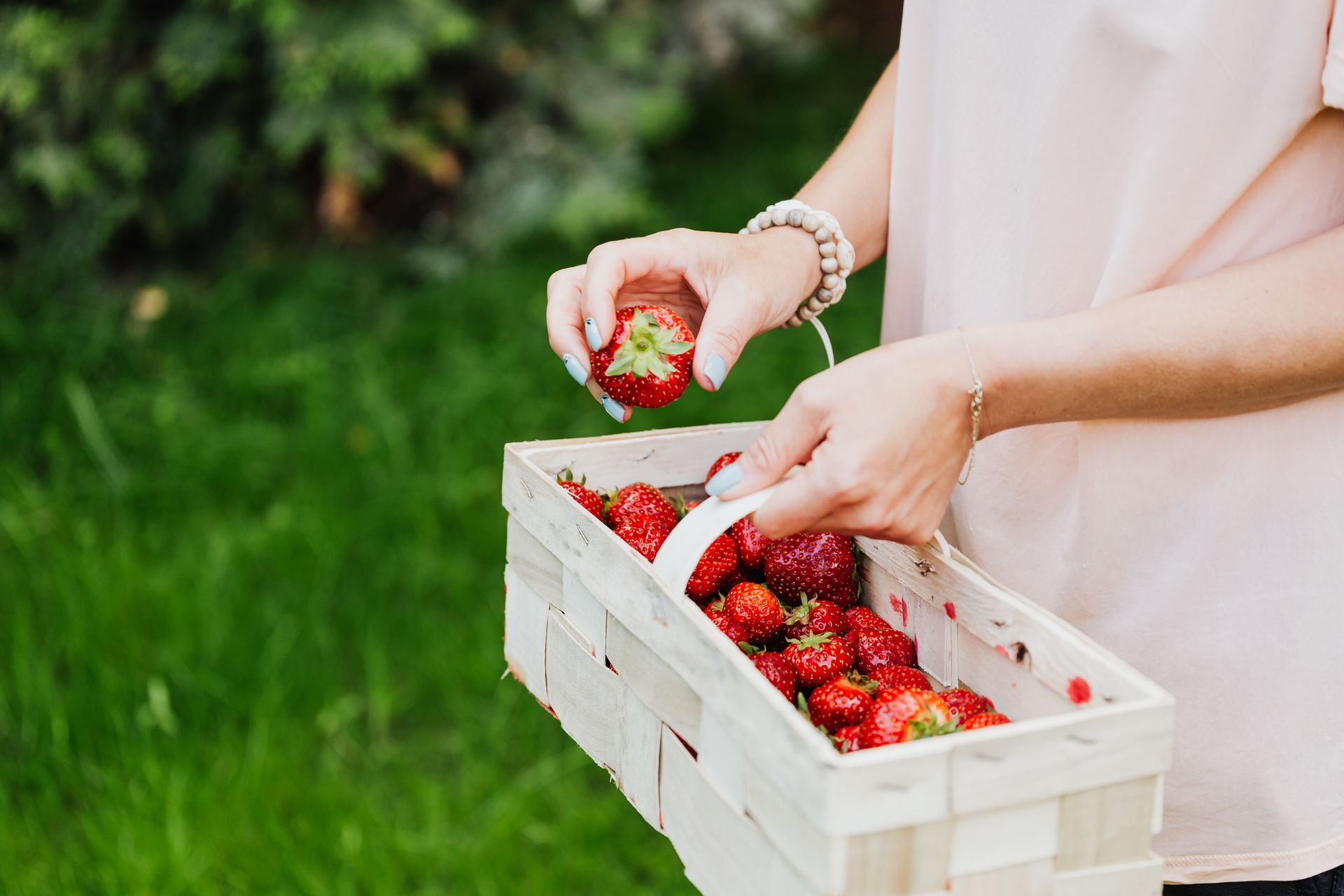A woman holding a basket full of fresh strawberries outdoors, symbolizes healthy living.