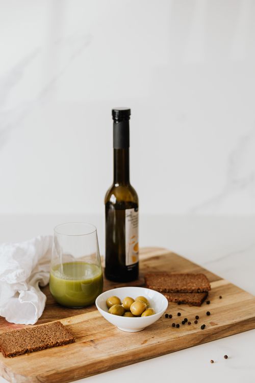 Free A cozy breakfast scene featuring green juice, olives, and rye bread on a wooden board. Stock Photo