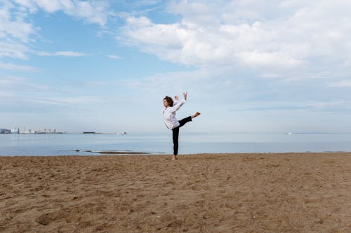 Free Woman in White Long Sleeve Shirt and Black Pants Standing on Brown Sand Stock Photo