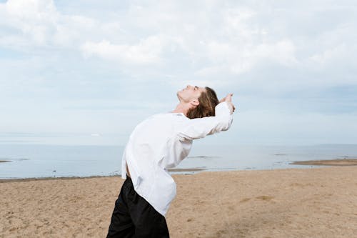 Free Woman in White Long Sleeve Shirt and Black Pants Standing on Brown Sand Stock Photo