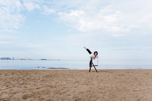 Free Man in White Shirt and Black Shorts Standing on Brown Sand Near Body of Water during Stock Photo