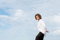 Woman in White Dress Shirt and Black Pants Standing on White Sand