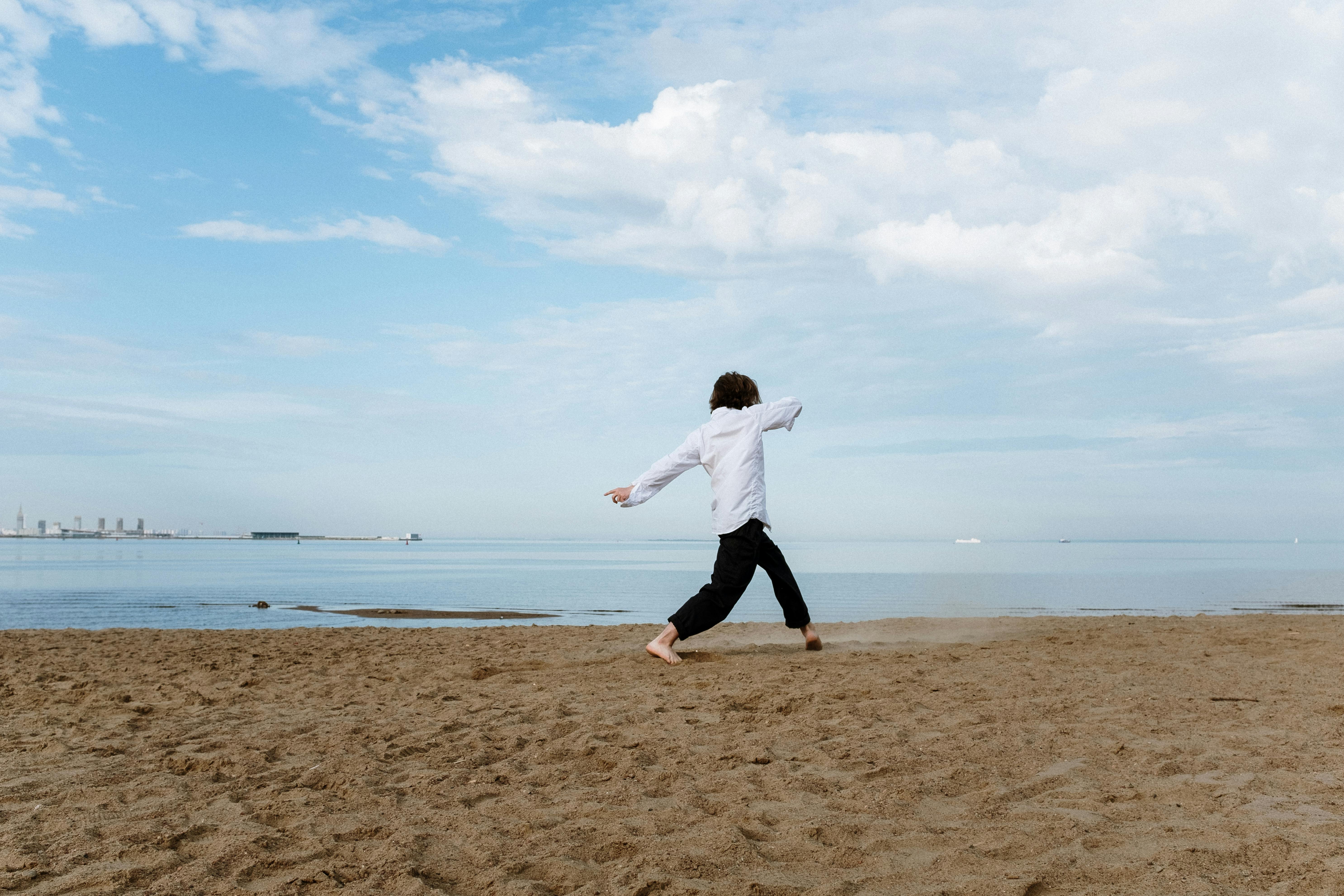 一名男子在沙滩上，以宁静的海洋和晴朗的蓝天为背景，表演当代舞蹈