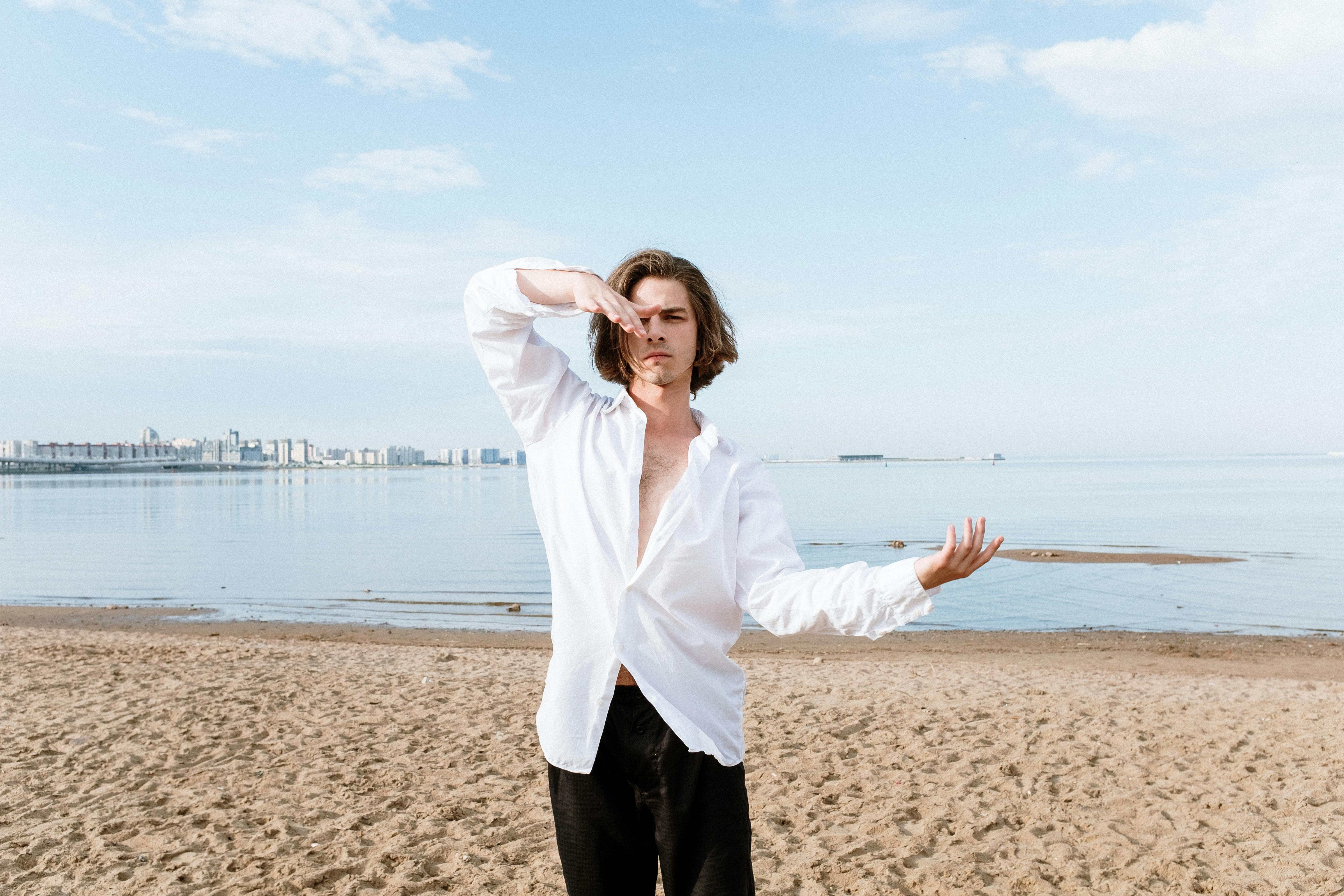 一名身穿白衬衫的男舞者，在城市天际线为背景的海滩上表演现代舞