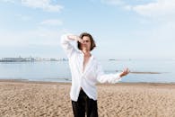 一名身穿白衬衫的男舞者，在城市天际线为背景的海滩上表演现代舞