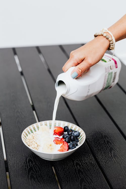 Hand Pouring Milk in White Ceramic Bowl