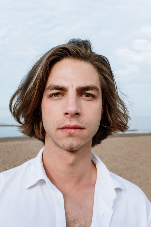 Free Close-up portrait of a man with long hair and heterochromia on a sandy beach under a blue sky. Stock Photo