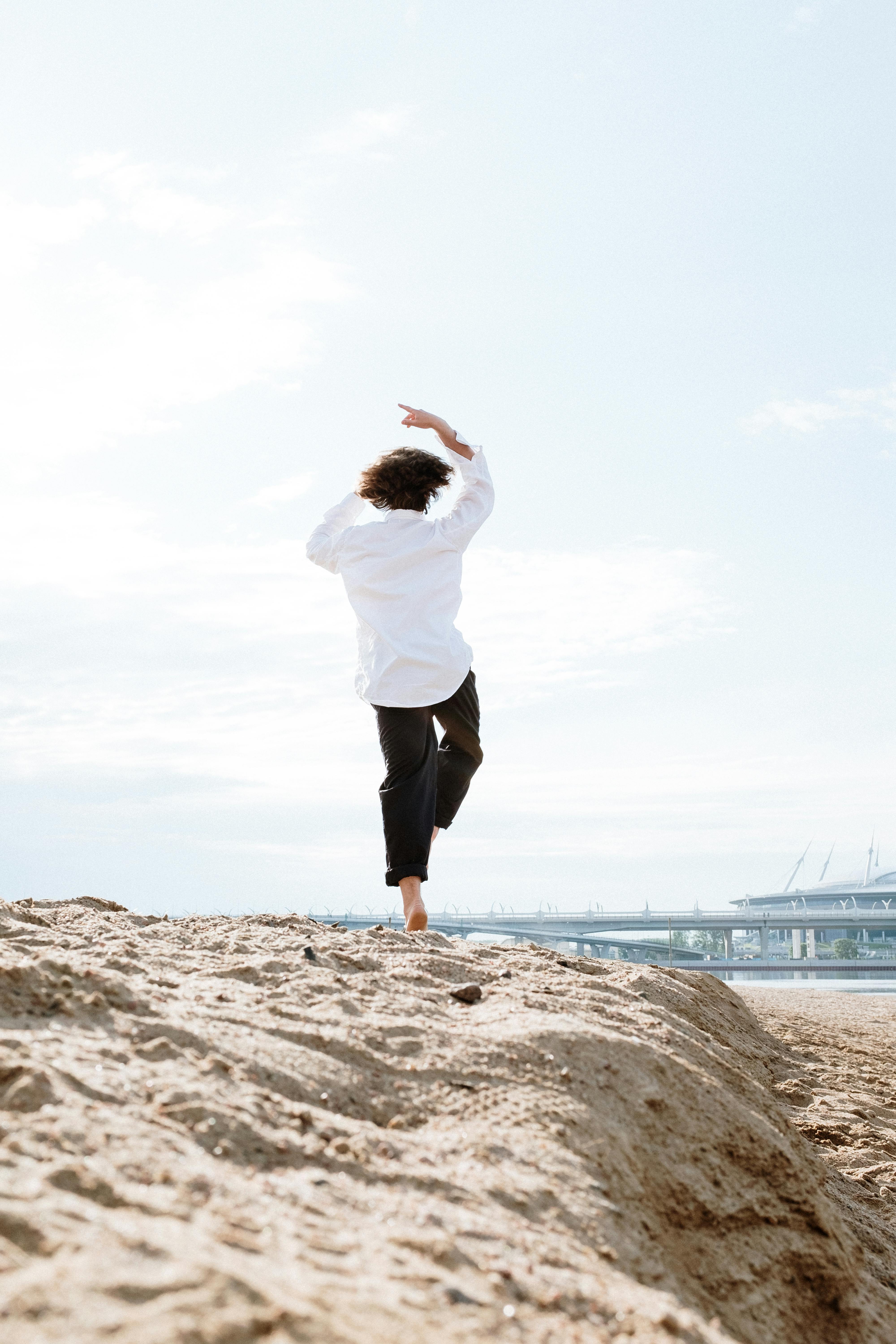 一名男子在晴朗天空下的沙滩上表演现代舞