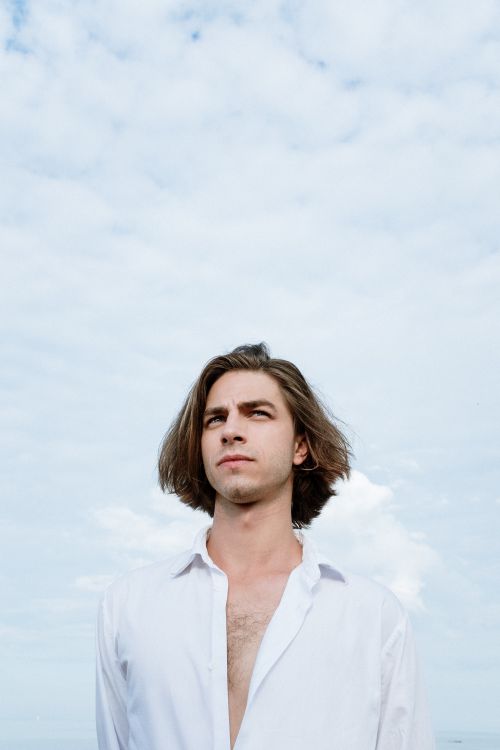Free Portrait of a young man outdoors under a bright, cloudy sky. Stock Photo