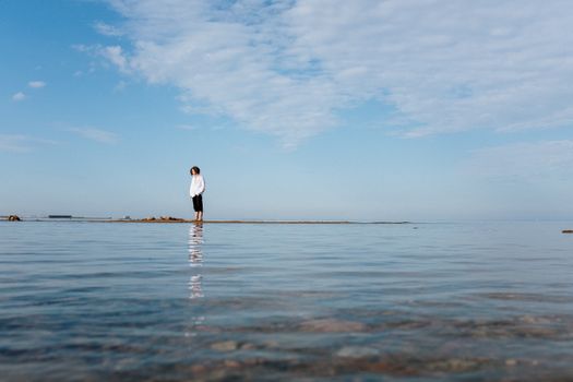 平静的海滩上，一个孤独的人站着，平静的蓝天倒映在水中