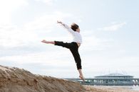 一位男舞者在沙滩上，以一座引人注目的现代桥梁为背景表演跳高