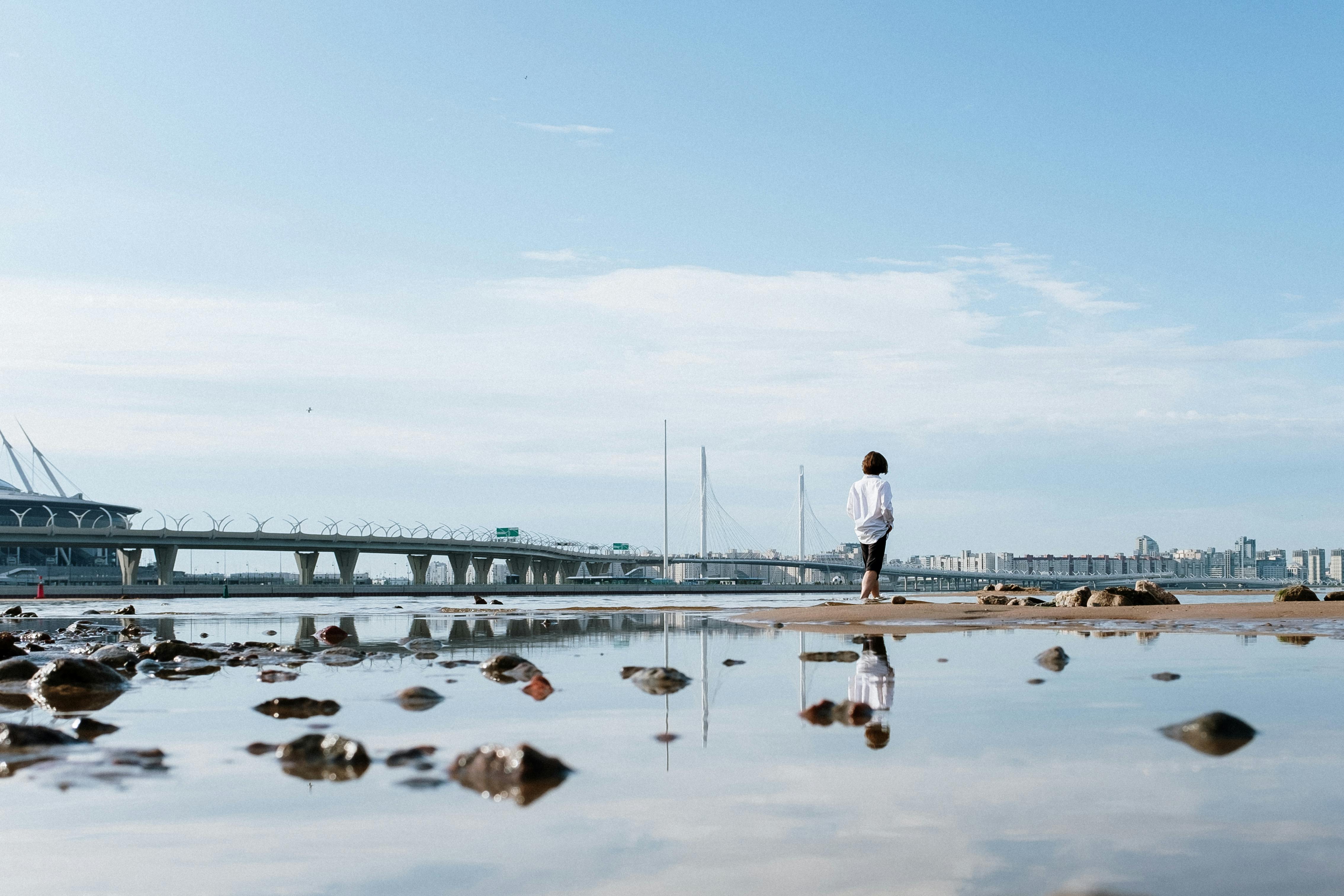 水面上站着一个孤独的人，倒映出远处的现代桥梁和城市景观