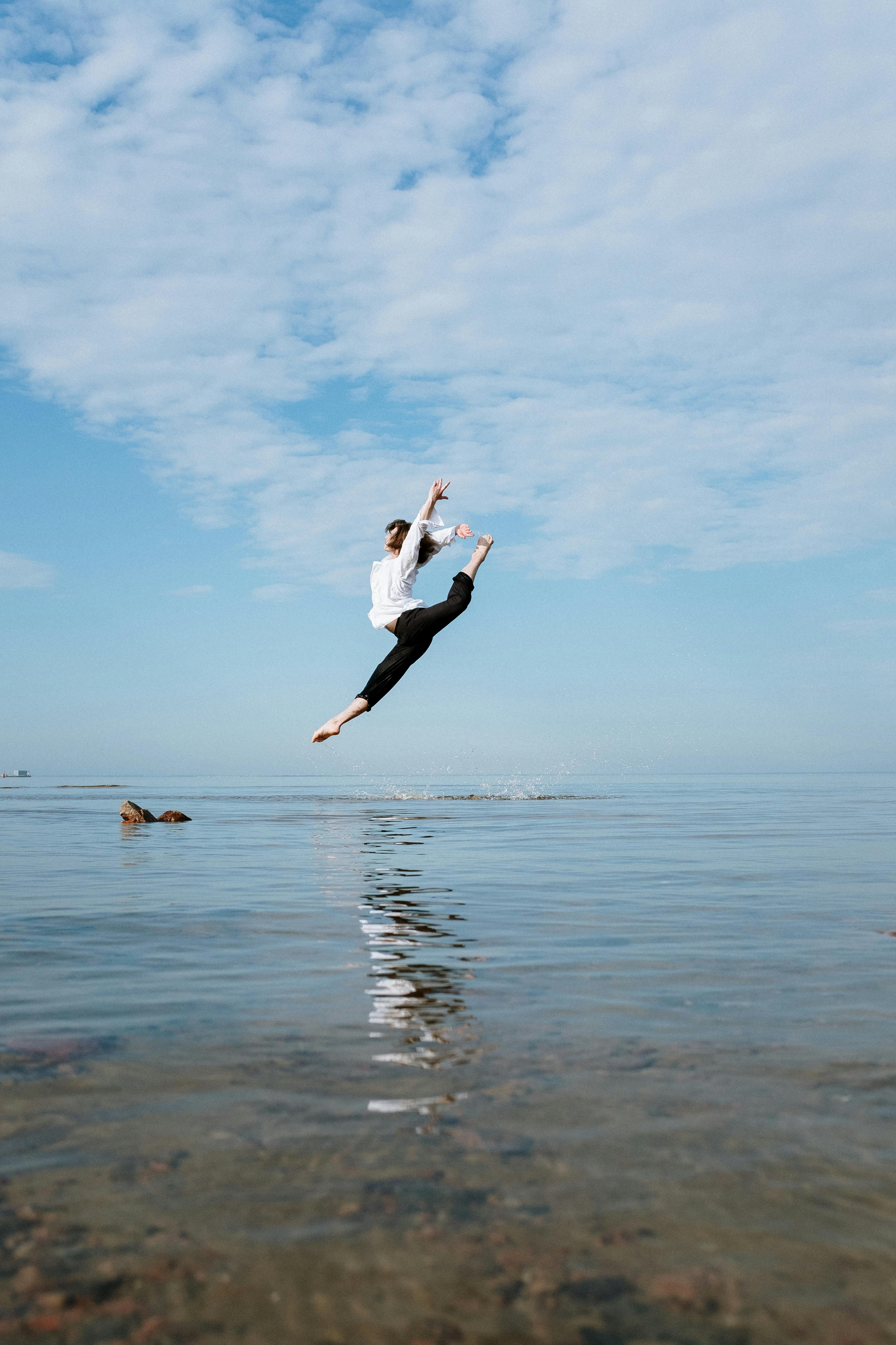 woman in white long sleeve shirt and black pants jumping on water