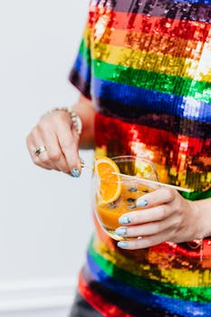 特写一位身穿活力彩虹连衣裙的人，手拿新鲜橙汁和装饰