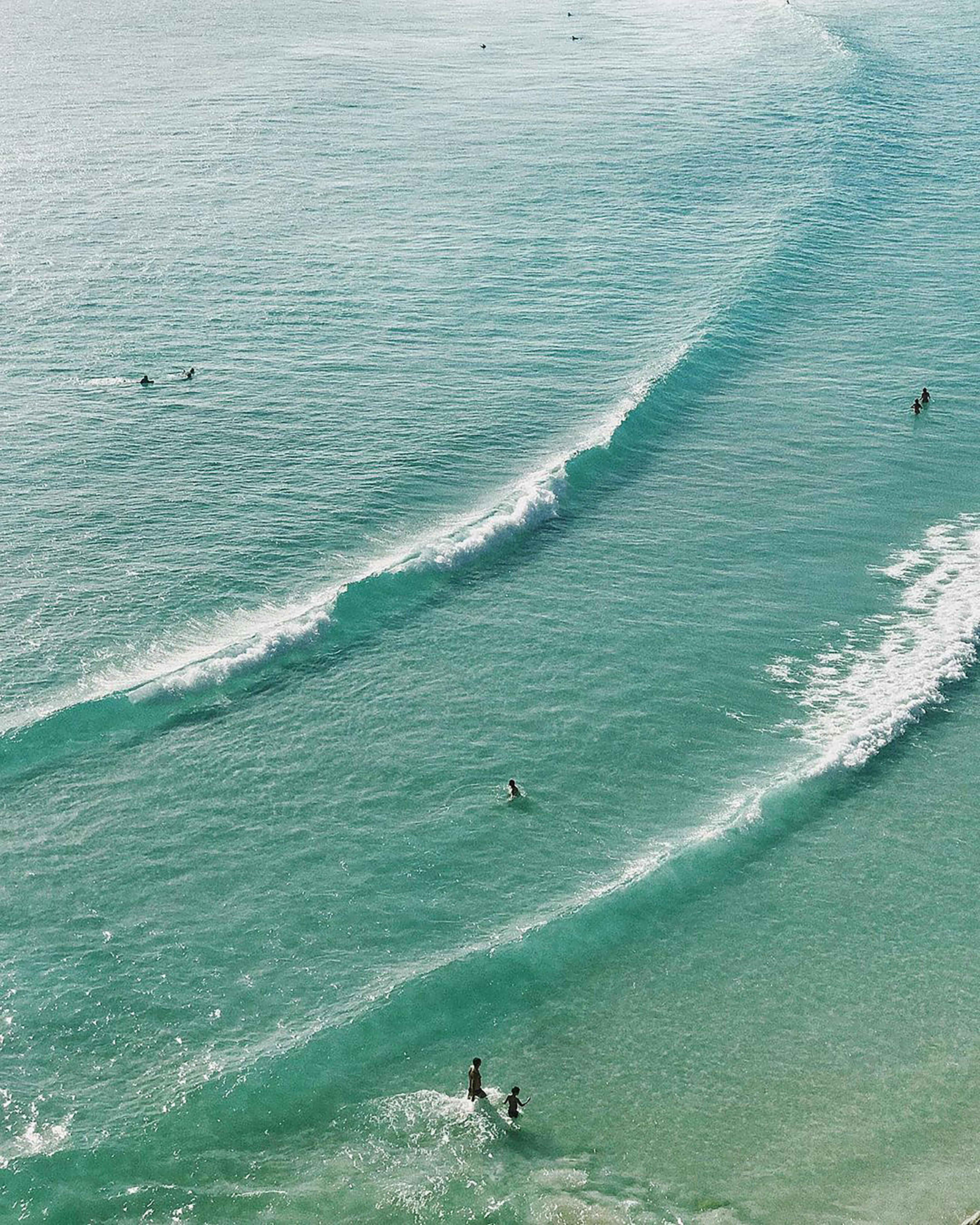 Aerial image of turquoise waters and beachgoers in Arraial do Cabo, Brazil, showcasing serene waves.