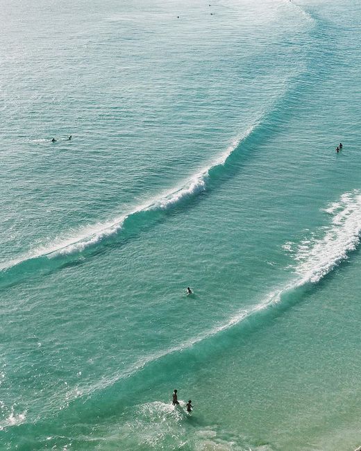 Aerial image of turquoise waters and beachgoers in Arraial do Cabo, Brazil, showcasing serene waves.