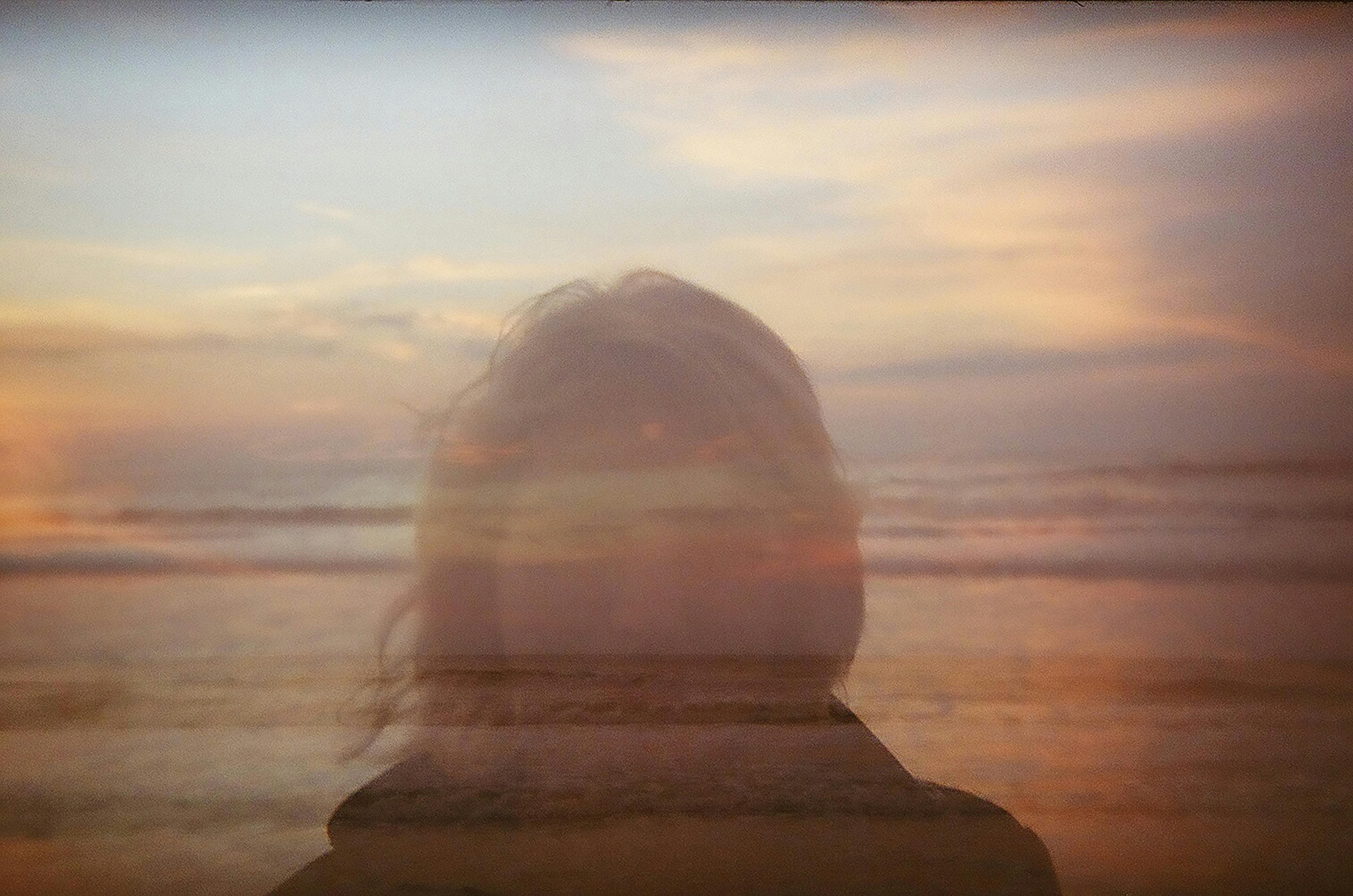 Artistic double exposure of a woman's silhouette with a sunset ocean view.