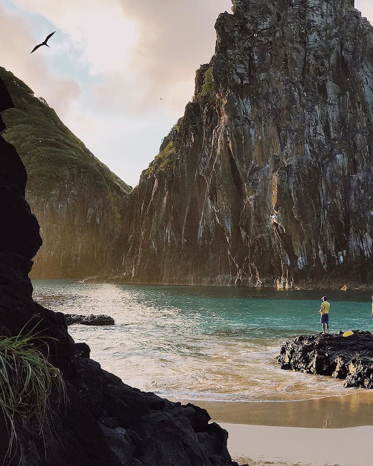 Person Standing In Front Of A Rock Formation On The Island Of Fernando De Noronha, Pernambuco, Brazil