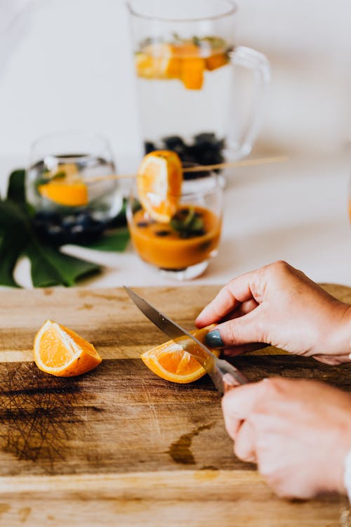 A Person Slicing Orange Fruit on a Wooden Chopping Board