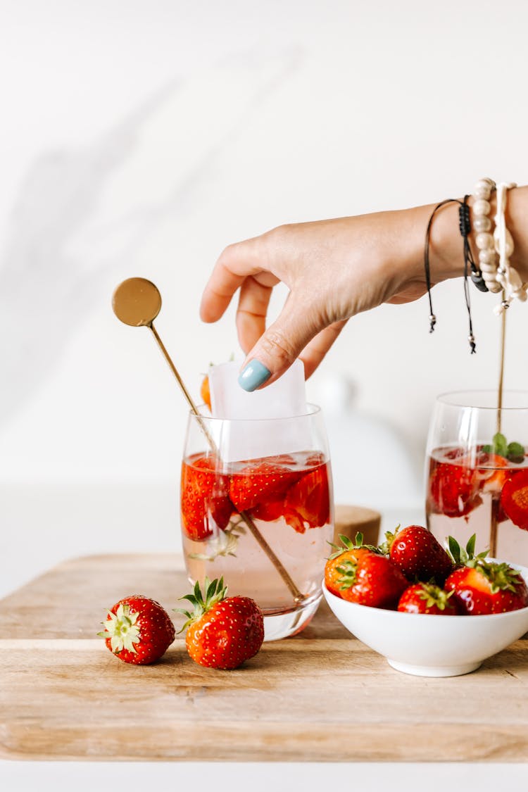 A Person Dropping Ice Cube In A Glass Of Drink With Strawberries 