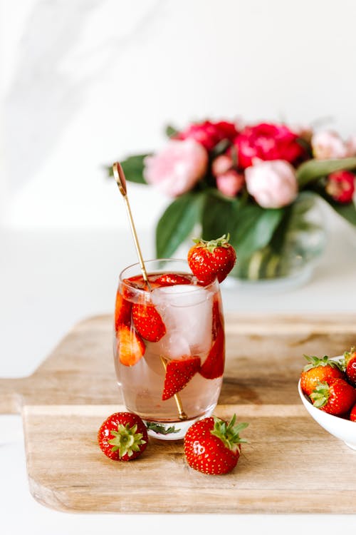 A Glass of Iced Drink with Strawberries on a Wooden Chopping Board
