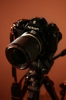 Close-up of a classic Nikon camera mounted on a tripod in a warm-toned studio.