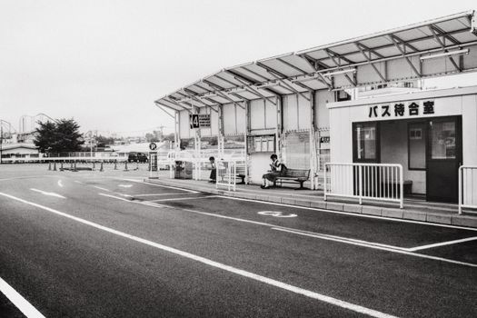 Black and white of empty asphalt roadway with marking lines and white fences on roadside with people sitting on benches