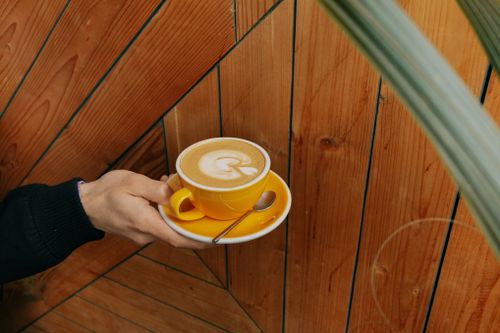 Free A person holds a yellow cup of cappuccino with latte art on a wooden background. Stock Photo