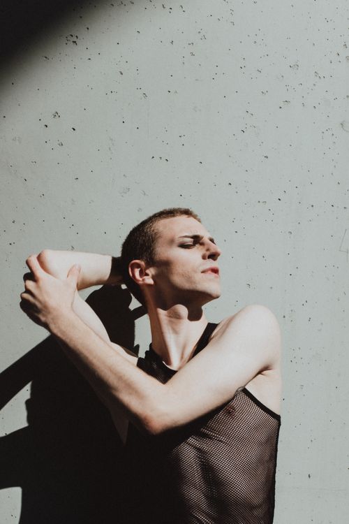 Free A fashionable young man in a mesh singlet striking a pose against a concrete wall. Stock Photo