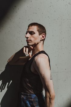 A fashionable man strikes a dramatic pose in sunlight, creating shadows on a concrete wall.