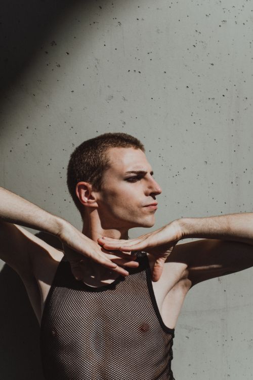 Free Profile of a male model in mesh singlet posing against concrete background with dramatic shadow play. Stock Photo