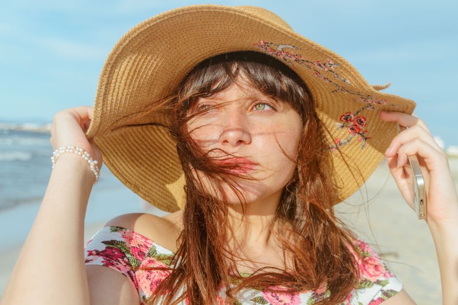 Young woman on the beach in a straw hat and floral top enjoying a sunny day.