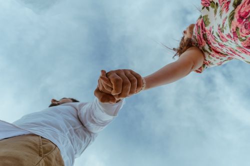 Free Low angle shot of a young couple holding hands with a vibrant sky backdrop, symbolizing love and togetherness. Stock Photo
