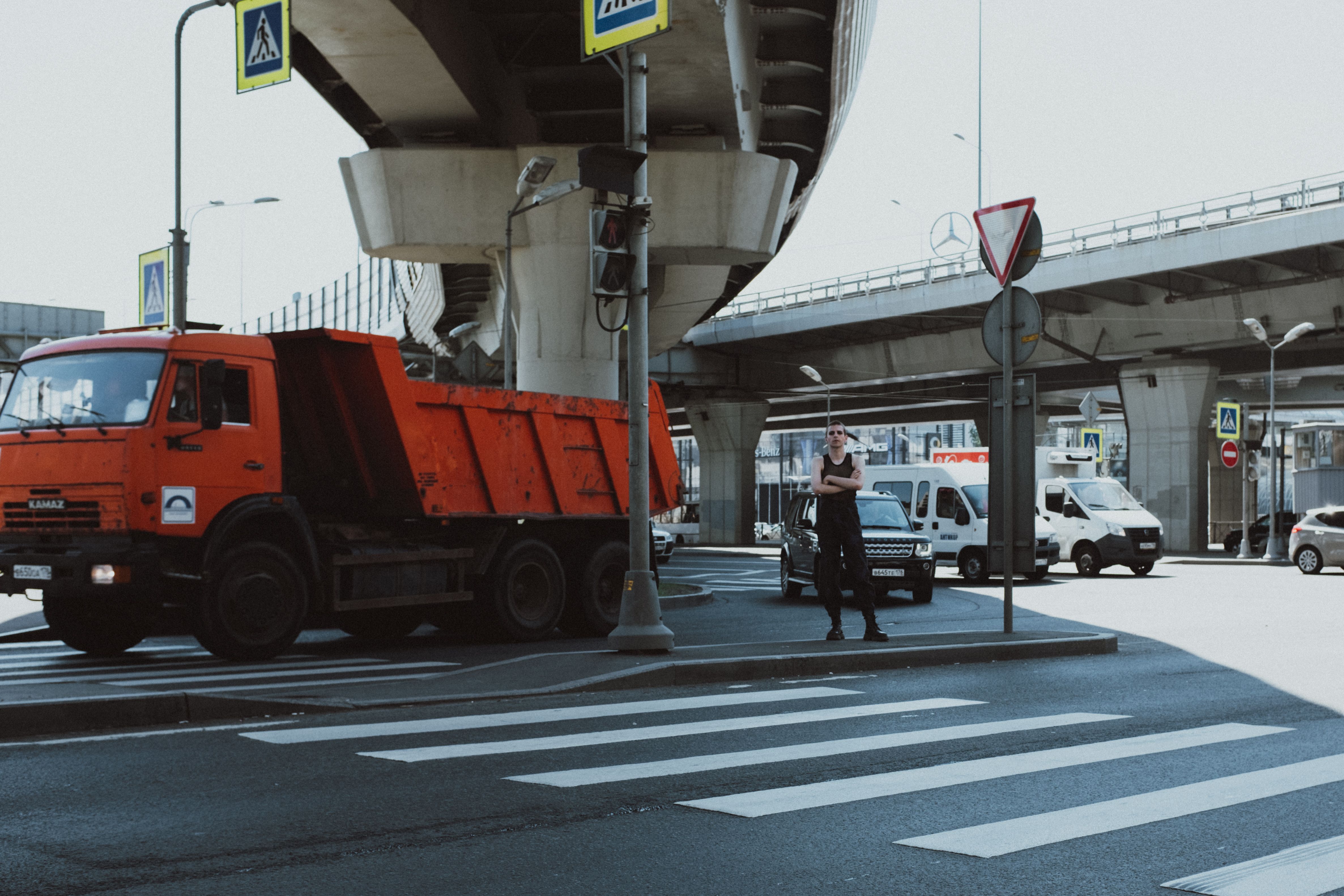 在明亮的日光下，城市交叉路口有一辆红色卡车、行人和一座立交桥