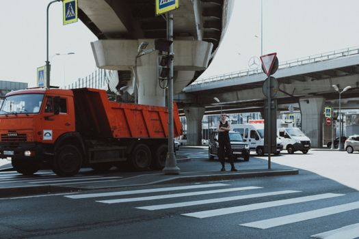 在明亮的日光下，城市交叉路口有一辆红色卡车、行人和一座立交桥