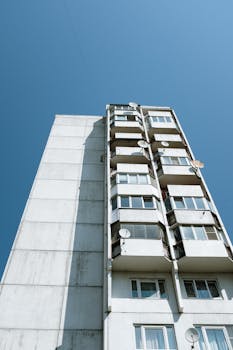Panel building facade with balconies and satellite dishes, captured against a clear blue sky. Urban architecture scene.