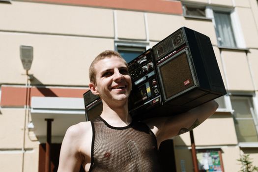 Smiling man with vintage boombox in urban setting, enjoying music outdoors.
