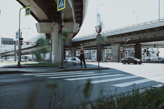 一名行人在城市立交桥下的人行横道上等候，车辆从旁驶过
